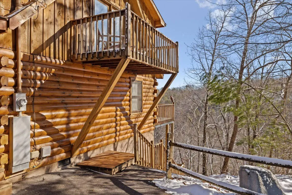 A stunning view of a log cabin structure with a balcony set against natural surroundings. The balcony offers a vantage point for sunset views or wildlife observation, reinforcing the feeling of seclusion and connection to the Smoky Mountain landscape.
