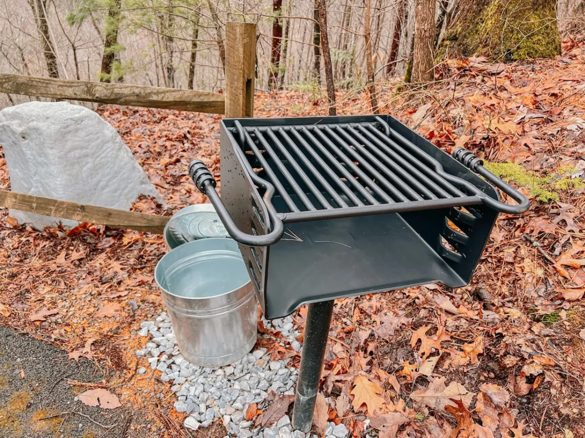 A dedicated grilling spot outdoors, featuring a charcoal grill set on gravel beneath the trees. The area is designed for barbecuing and picnicking in a relaxed, social environment, making it perfect for families and friends to gather and enjoy meals after a day of mountain adventures.
