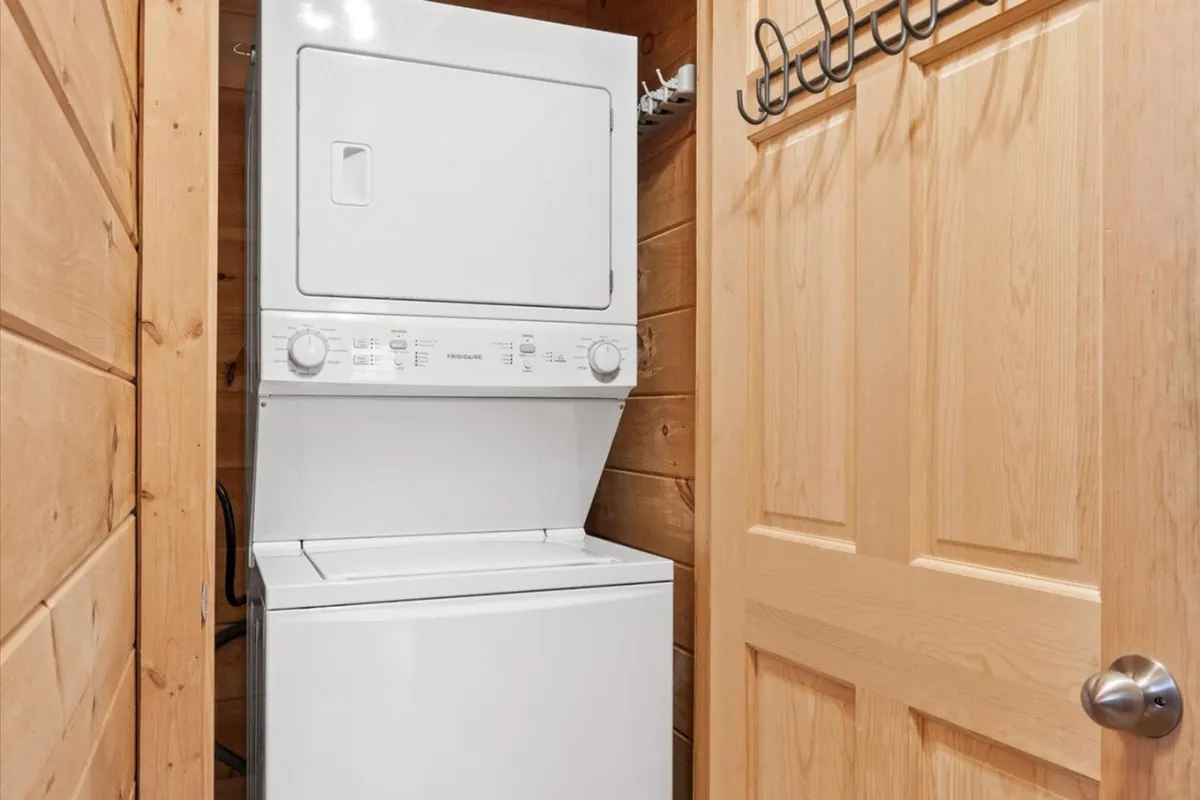 A utility area featuring a stacked washer and dryer, a wooden door, and practical hanging hooks for organization. The space reflects thoughtful amenities for guests’ convenience during their stay.