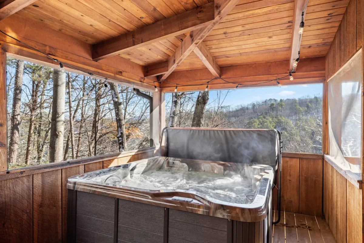This image captures a tranquil hot tub area nestled within a wooden structure, surrounded by lush trees visible through the screened openings. The intimate setting is perfect for relaxing and soaking in the natural forest ambiance, connecting the comfort of indoors with the beauty of the outdoors.