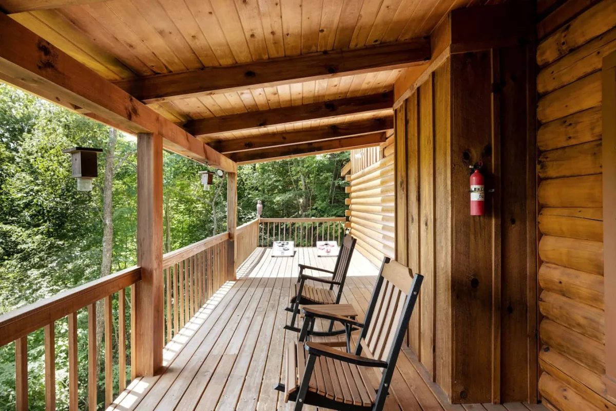 A welcoming outdoor deck furnished with classic wooden rocking chairs overlooks thick greenery. The space is decorated with lanterns and features a sturdy wooden railing, inviting guests to enjoy morning coffee, wildlife watching, or sunset views in a relaxed, screened-in setting.