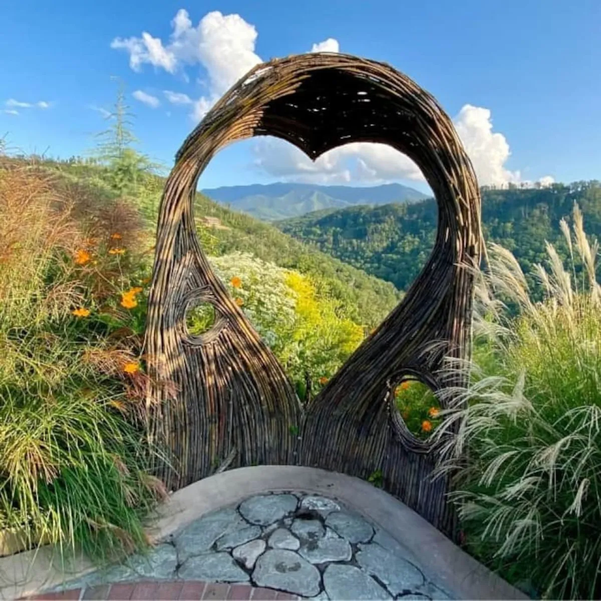 A heart-shaped archway frames lush greenery and a distant mountain view, creating a naturally romantic setting. The scene invites couples to take a stroll, capture memorable photos, or simply pause to enjoy the serenity and beauty of the outdoors together.