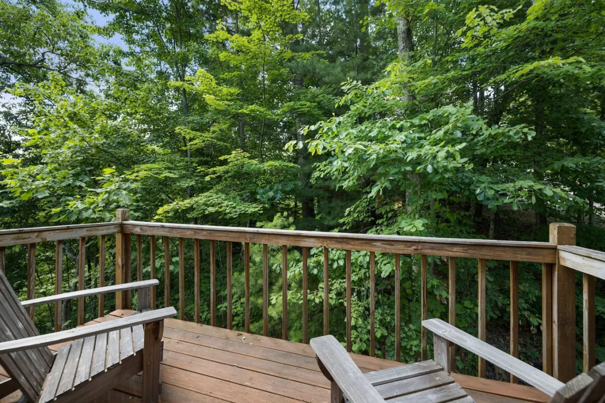 A wooden deck surrounded by lush greenery, featuring two chairs positioned perfectly for relaxing and soaking in the natural environment. The scene feels peaceful, with the deck appearing as an inviting spot to enjoy the outdoors, sip tea, or watch the sunrise or sunset.
