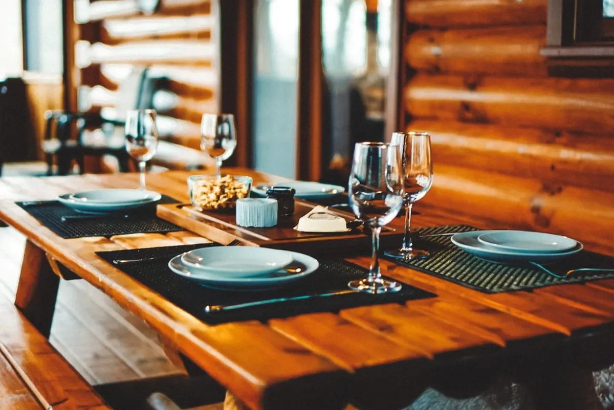 A close-up view of a wooden dining table elegantly set with dinnerware, wine glasses, and a snack platter, creating a ready-to-entertain mood. The kitchen is visible in the background, hinting at the convenience and sociability of the space.